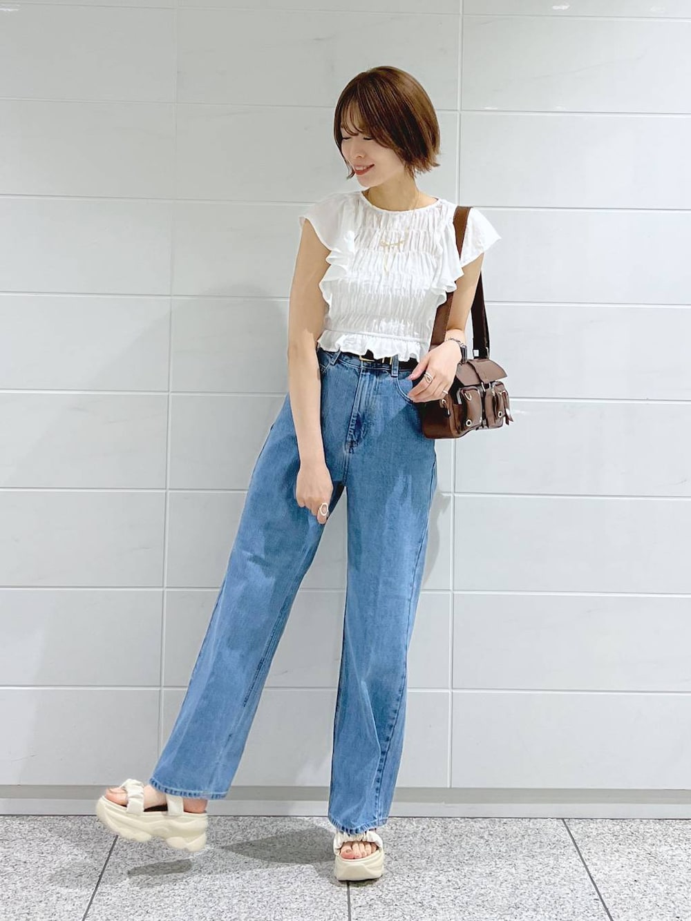 ブルー系のデニムパンツ、ホワイト系のサンダル、ブラウン系のショルダーバッグを着用したレディースの春コーディネートの1枚目の写真