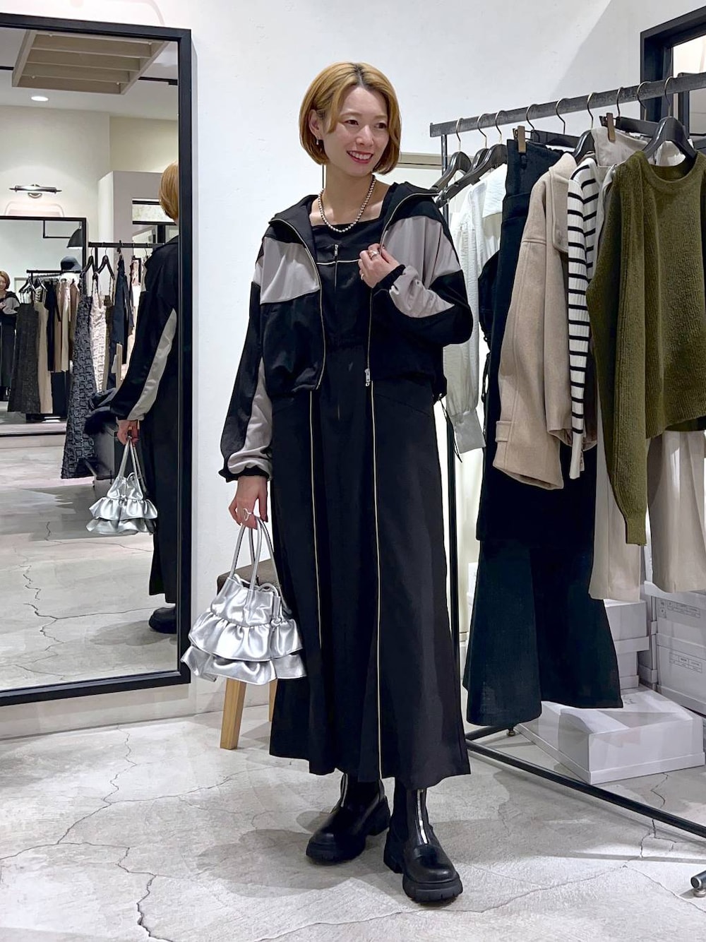 シルバー系のショルダーバッグ、ブラック系のブーツ、ブラック系のワンピースを着用したレディースの秋コーディネートの1枚目の写真