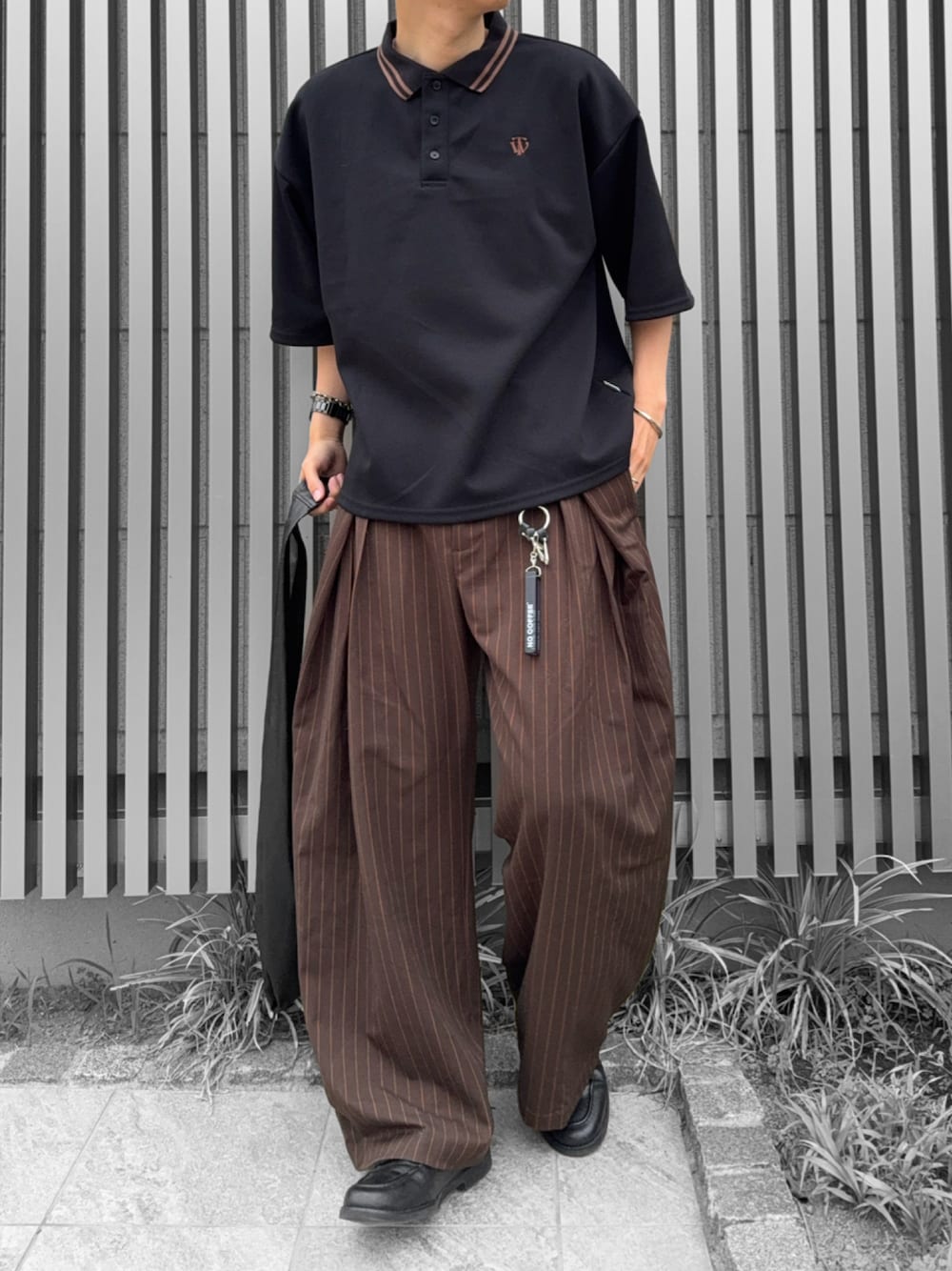 ブラック系のトートバッグ、ブラック系のポロシャツ、ブラウン系のスラックスを着用したメンズの夏コーディネートの1枚目の写真