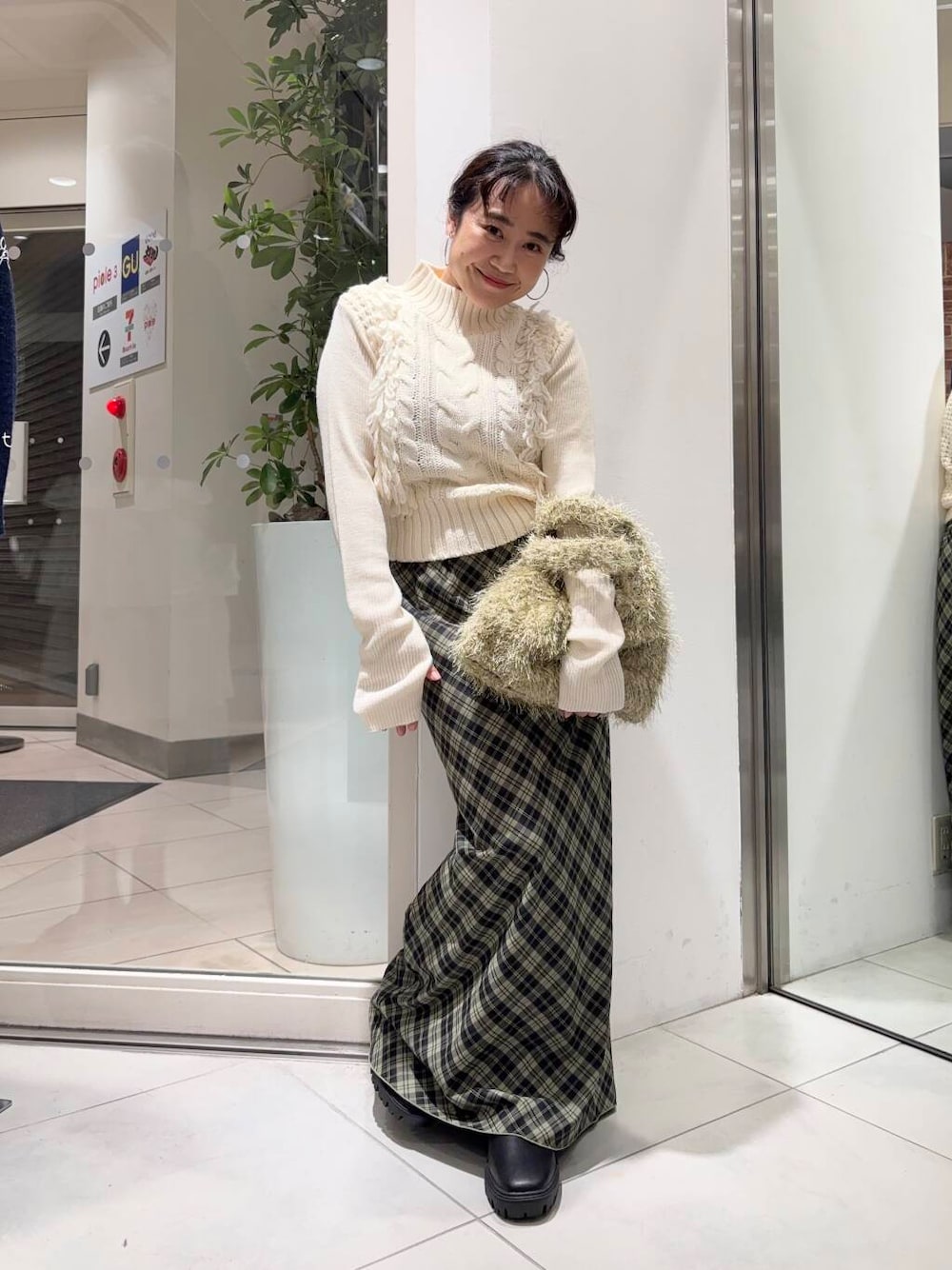 ブラック系のブーツ、ベージュ系のトートバッグ、グリーン系のスカートを着用したレディースの冬コーディネートの1枚目の写真