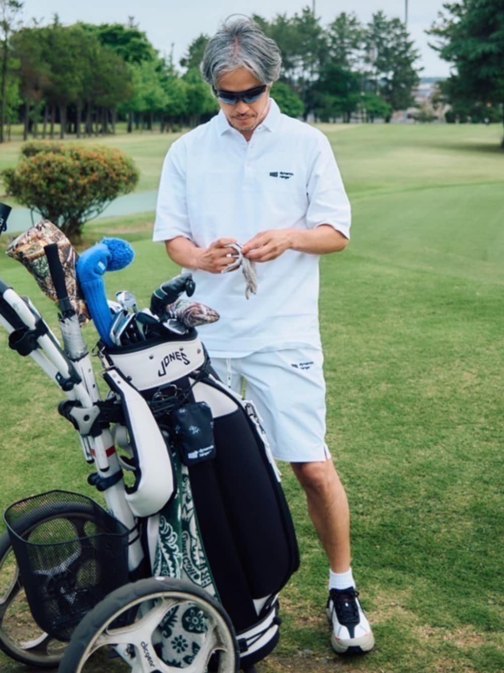 ホワイト系のポロシャツ、ホワイト系のその他パンツ、ブラック系のゴルフグッズを着用したメンズの夏コーディネートの1枚目の写真