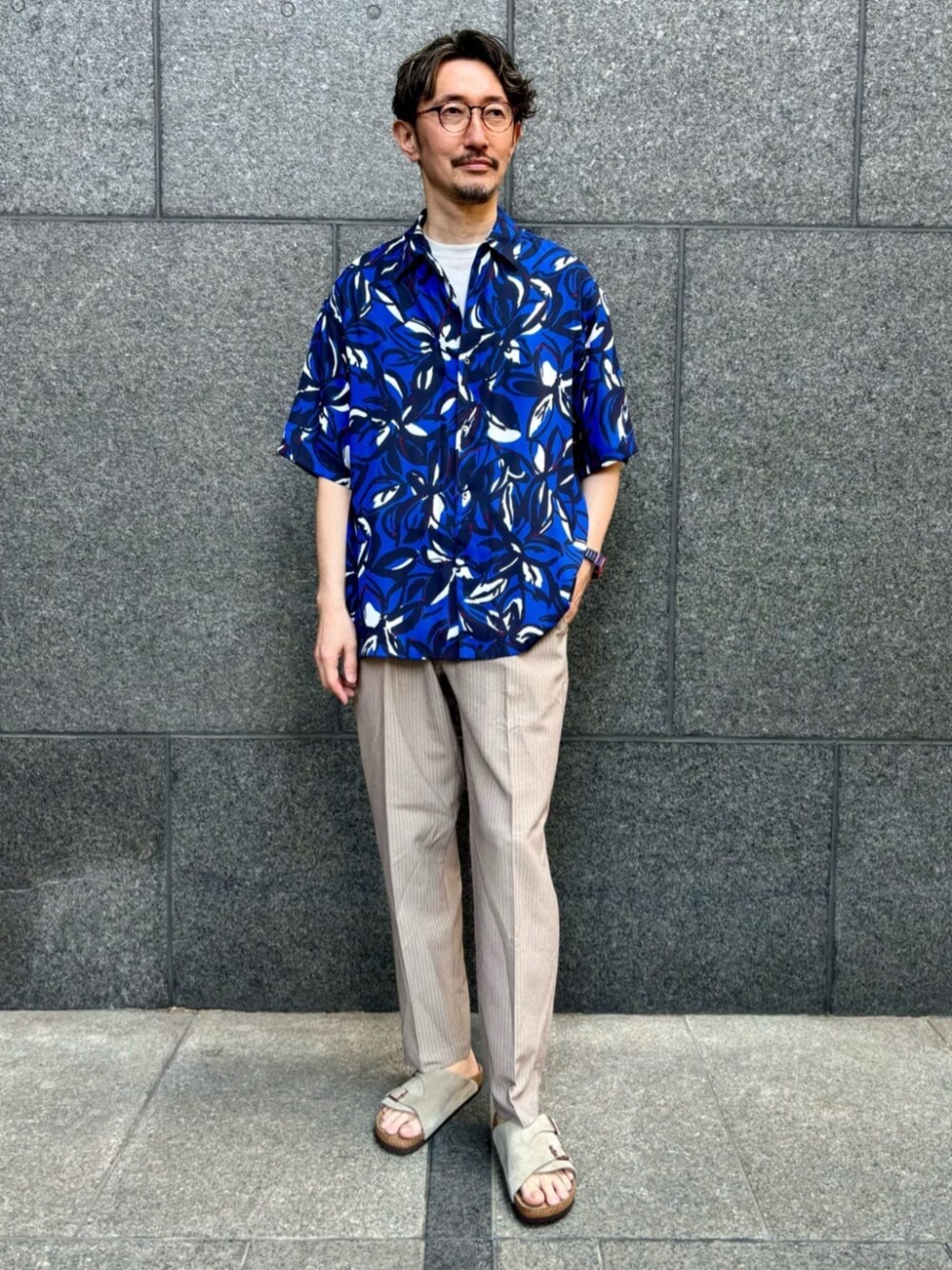 ブルー系のシャツ/ブラウス、ベージュ系のスラックス、ベージュ系のサンダルを着用したメンズの夏コーディネートの1枚目の写真