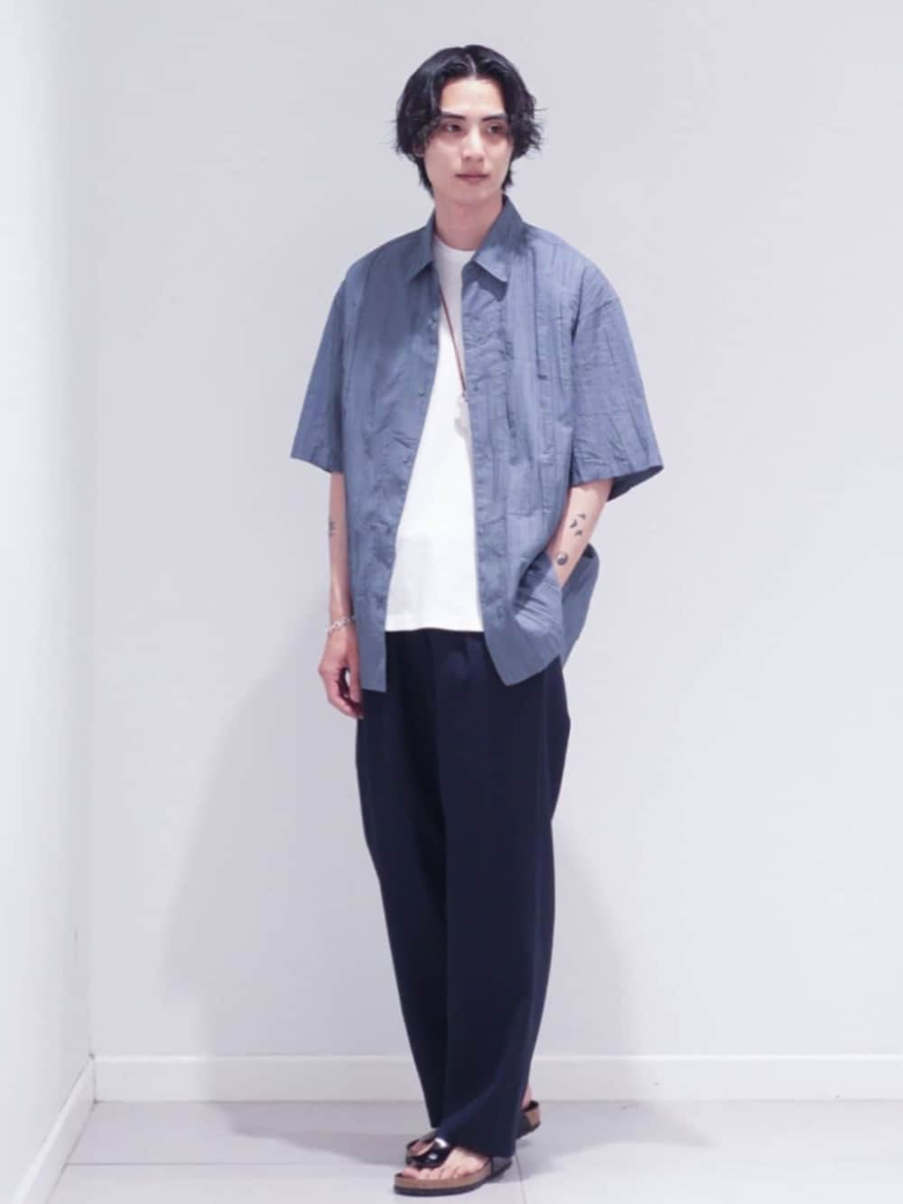 ホワイト系のTシャツ/カットソー、ブラック系のサンダル、ブルー系のスラックスを着用したメンズの夏コーディネートの1枚目の写真