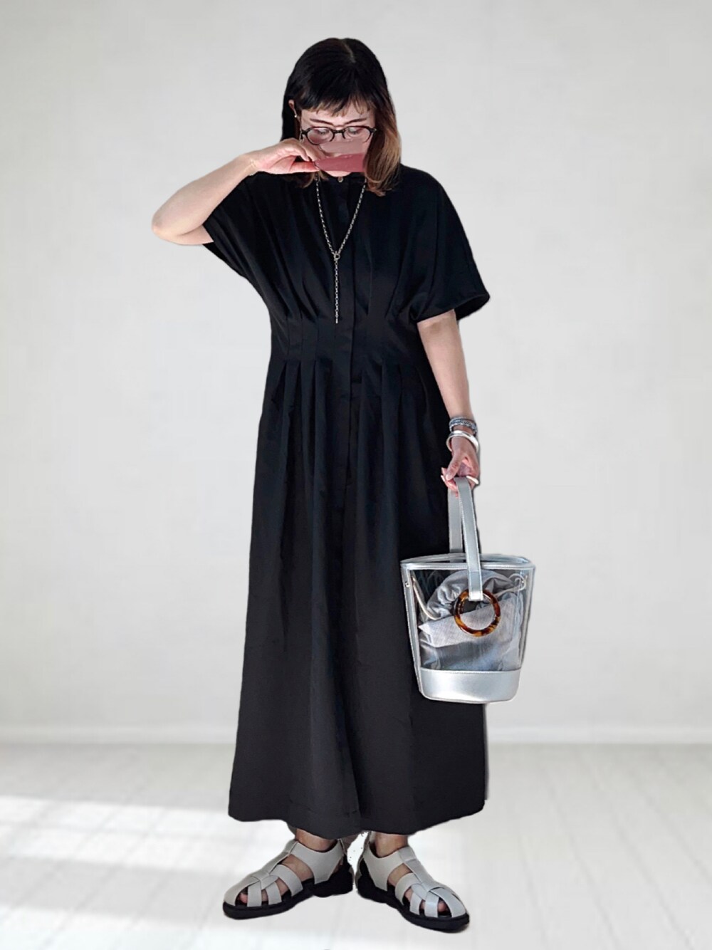 ブラック系のワンピース、シルバー系のショルダーバッグ、ホワイト系のサンダルを着用したレディースの夏コーディネートの1枚目の写真