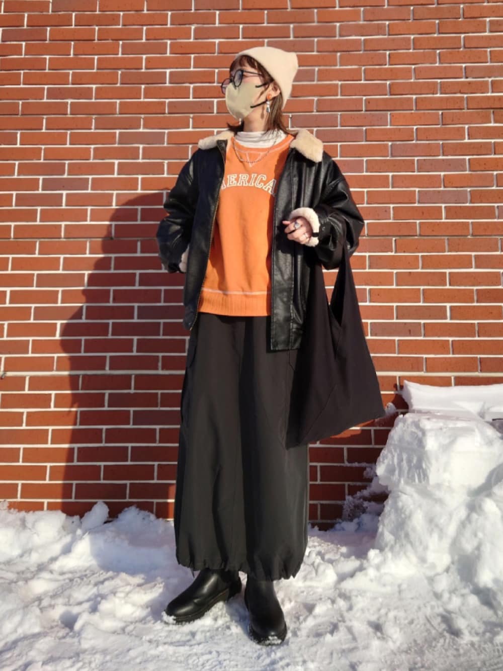 ブラック系のブルゾン、オレンジ系のスウェット、ホワイト系のTシャツ/カットソーを着用したレディースの冬コーディネートの1枚目の写真