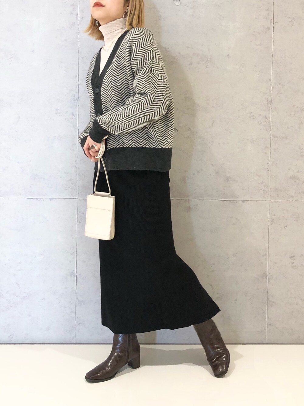 ブラック系のスカート、ブラウン系のブーツ、ホワイト系のショルダーバッグを着用したレディースの冬コーディネートの2枚目の写真
