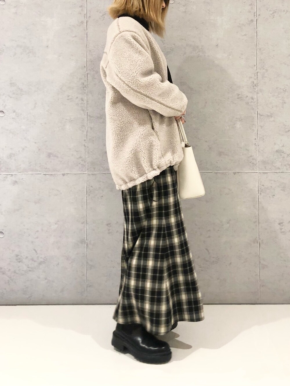 ブラック系のスカート、ブラック系のブーツ、ベージュ系のノーカラーコートを着用したレディースの冬コーディネートの2枚目の写真