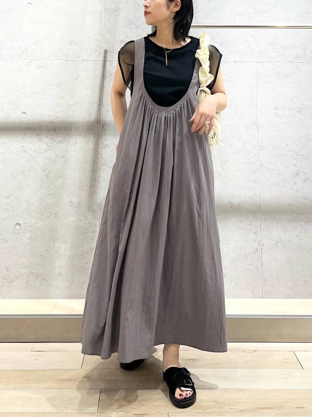 ブラック系のサンダル、グレー系のジャンパースカート、ホワイト系のショルダーバッグを着用したレディースの夏コーディネートの1枚目の写真