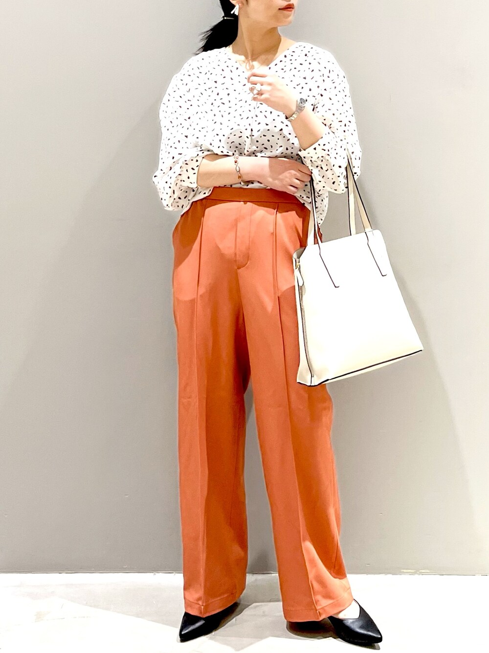 ホワイト系のシャツ/ブラウス、オレンジ系のスラックス、ブラック系のパンプスを着用したレディースの秋コーディネートの1枚目の写真