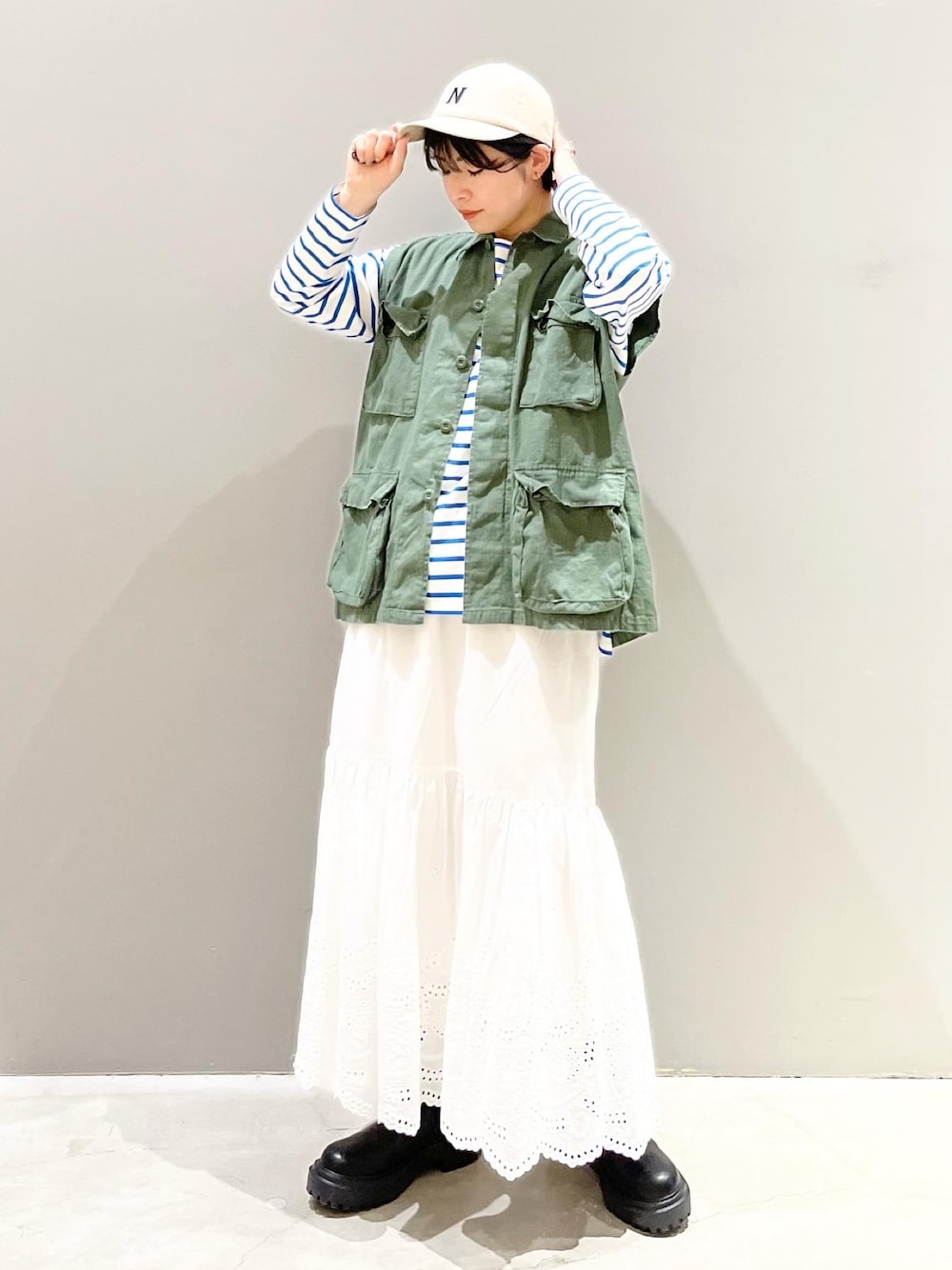 ブラック系のブーツ、ブルー系のTシャツ/カットソー、グリーン系のベストを着用したレディースの春コーディネートの1枚目の写真