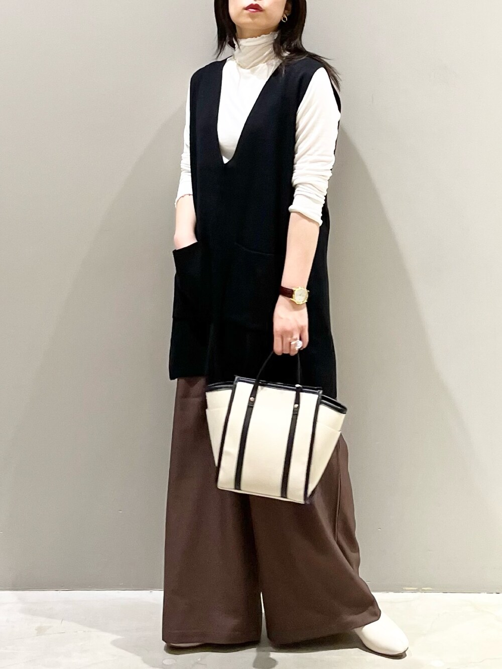 ホワイト系のショルダーバッグ、ブラック系のベスト、ブラック系のトップスを着用したレディースの秋コーディネートの1枚目の写真