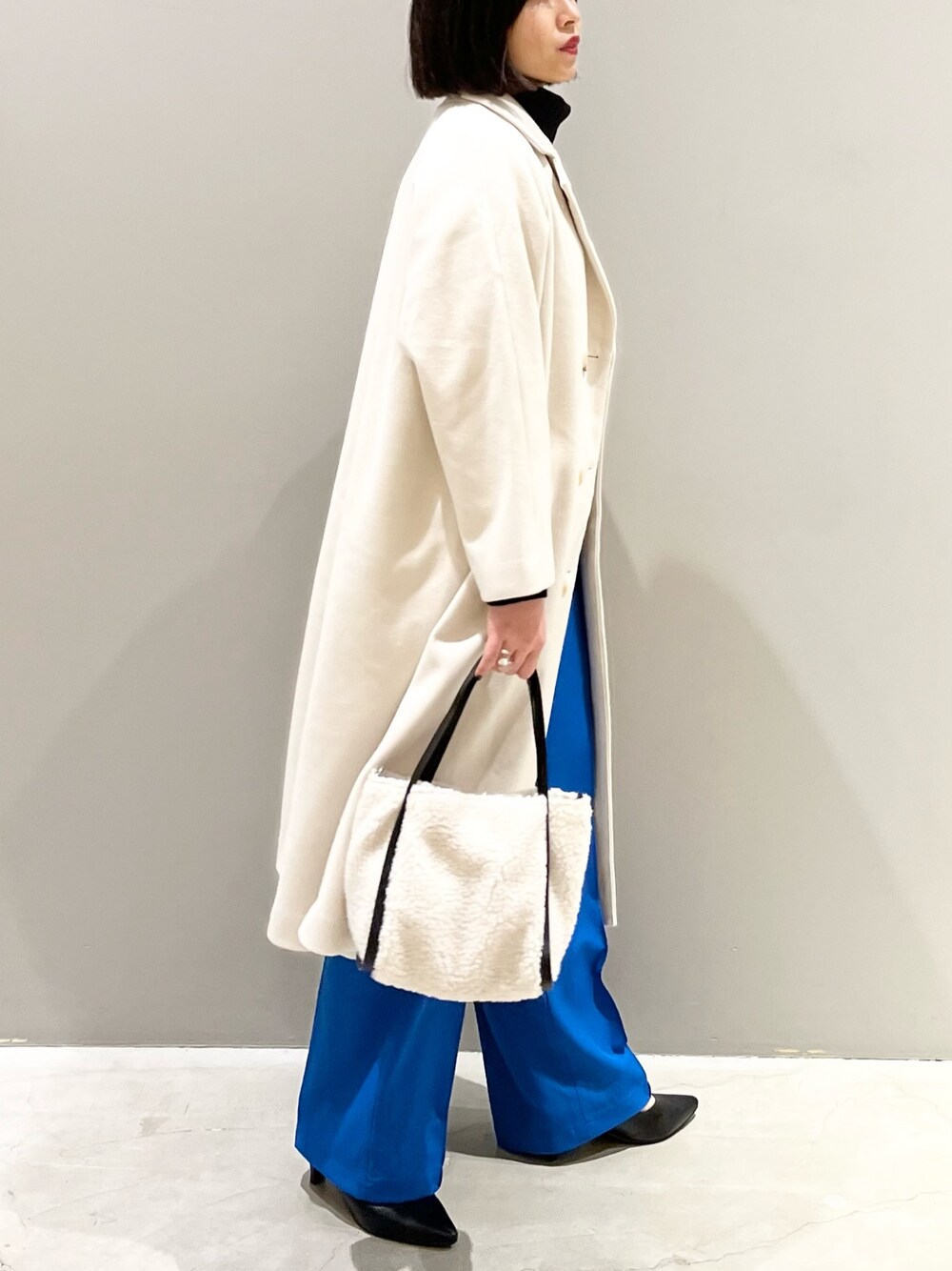 ホワイト系のチェスターコート、ブルー系のスラックス、ホワイト系のバッグを着用したレディースの冬コーディネートの1枚目の写真