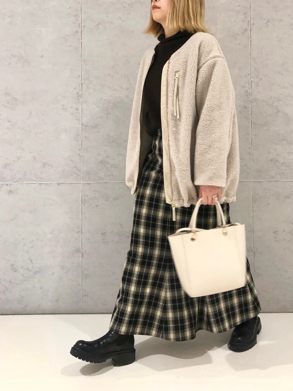 ブラック系のスカート、ブラック系のブーツ、ベージュ系のノーカラーコートを着用したレディースの冬コーディネートの4枚目の写真