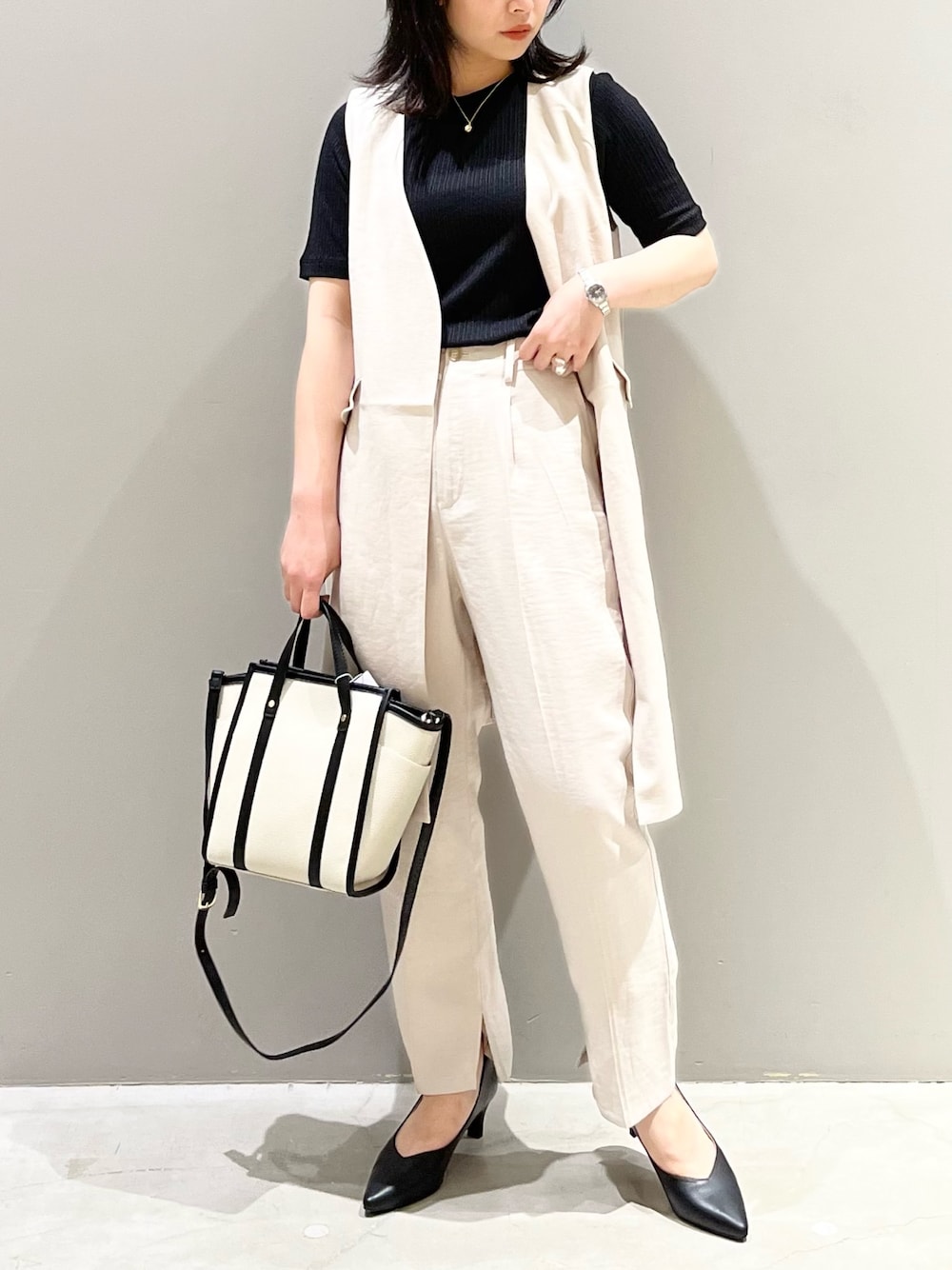 グレー系のパンツ、ブラック系のパンプス、ホワイト系のバッグを着用したレディースの夏コーディネートの2枚目の写真