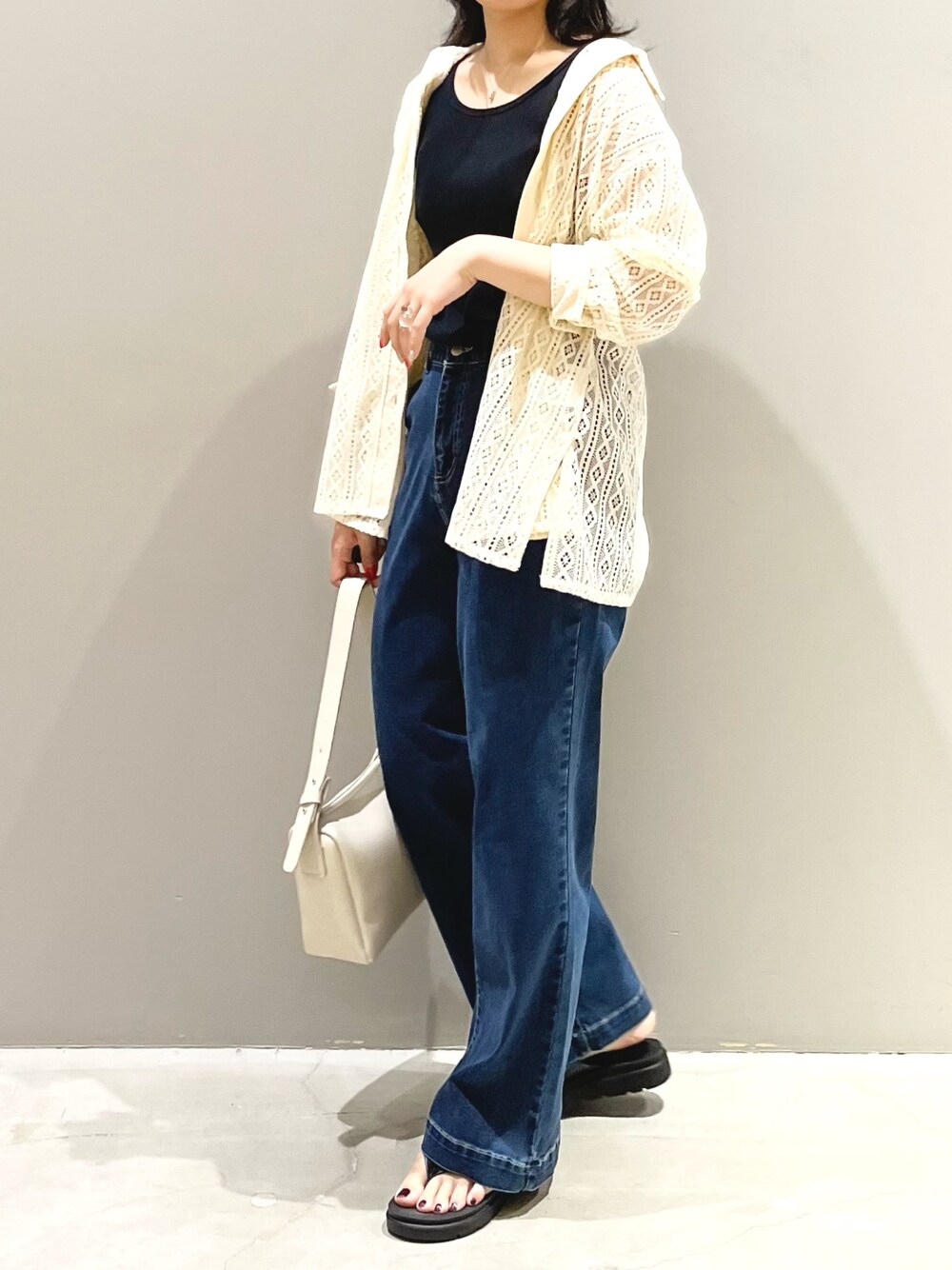 ブルー系のデニムパンツ、ホワイト系のショルダーバッグ、ブラック系のサンダルを着用したレディースの夏コーディネートの2枚目の写真