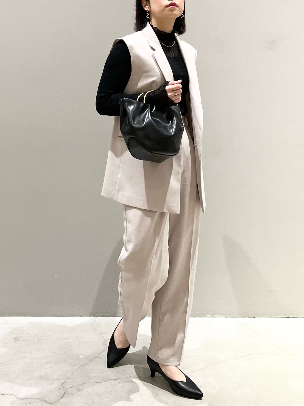 ブラック系のパンプス、ベージュ系のスラックス、ブラック系のハンドバッグを着用したレディースの冬コーディネートの1枚目の写真