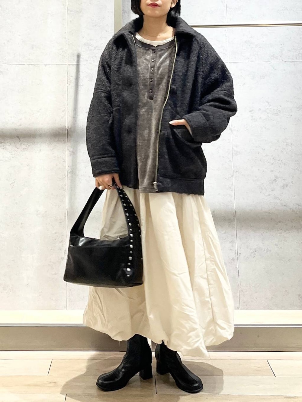 ブラック系のブーツ、ベージュ系のスカート、ブラック系のハンドバッグを着用したレディースの冬コーディネートの1枚目の写真