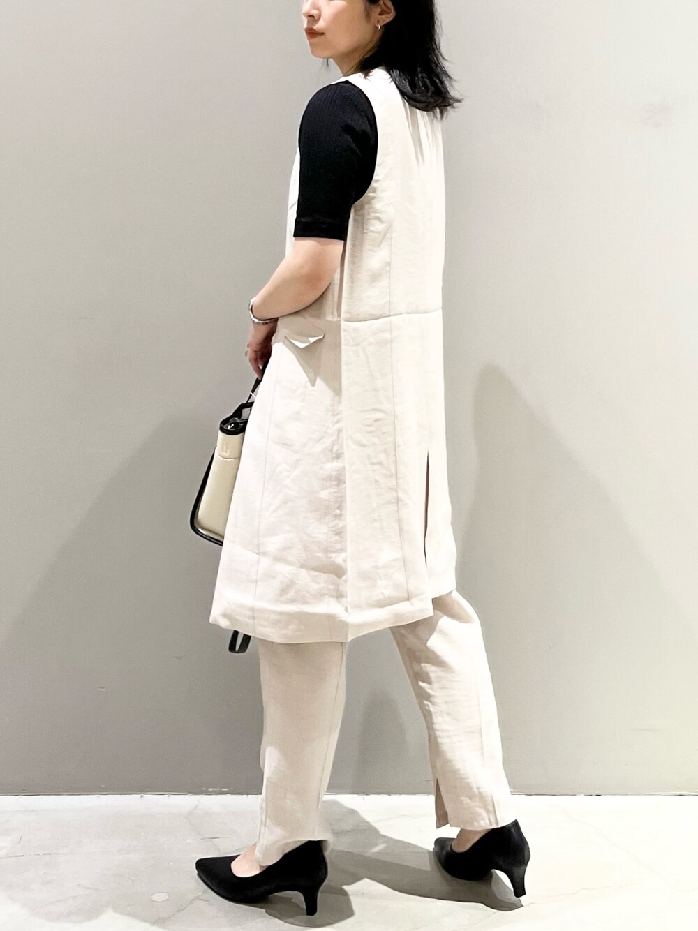 グレー系のパンツ、ブラック系のパンプス、ホワイト系のバッグを着用したレディースの夏コーディネートの4枚目の写真