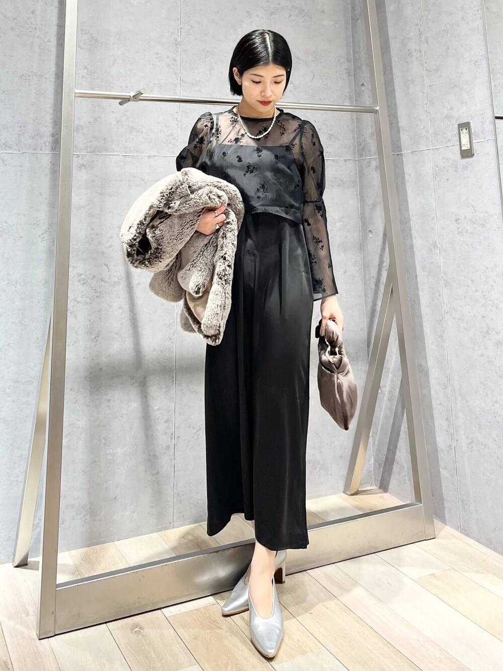 シルバー系のパンプス、ブラウン系のハンドバッグ、ベージュ系のノーカラーコートを着用したレディースの秋コーディネートの1枚目の写真