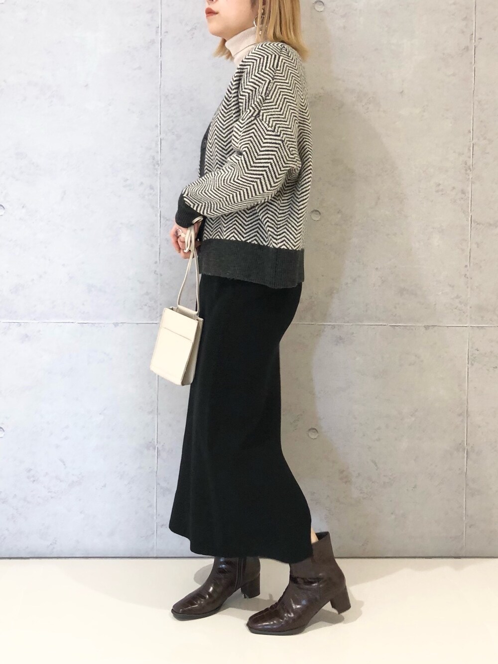 ブラック系のスカート、ブラウン系のブーツ、ホワイト系のショルダーバッグを着用したレディースの冬コーディネートの3枚目の写真