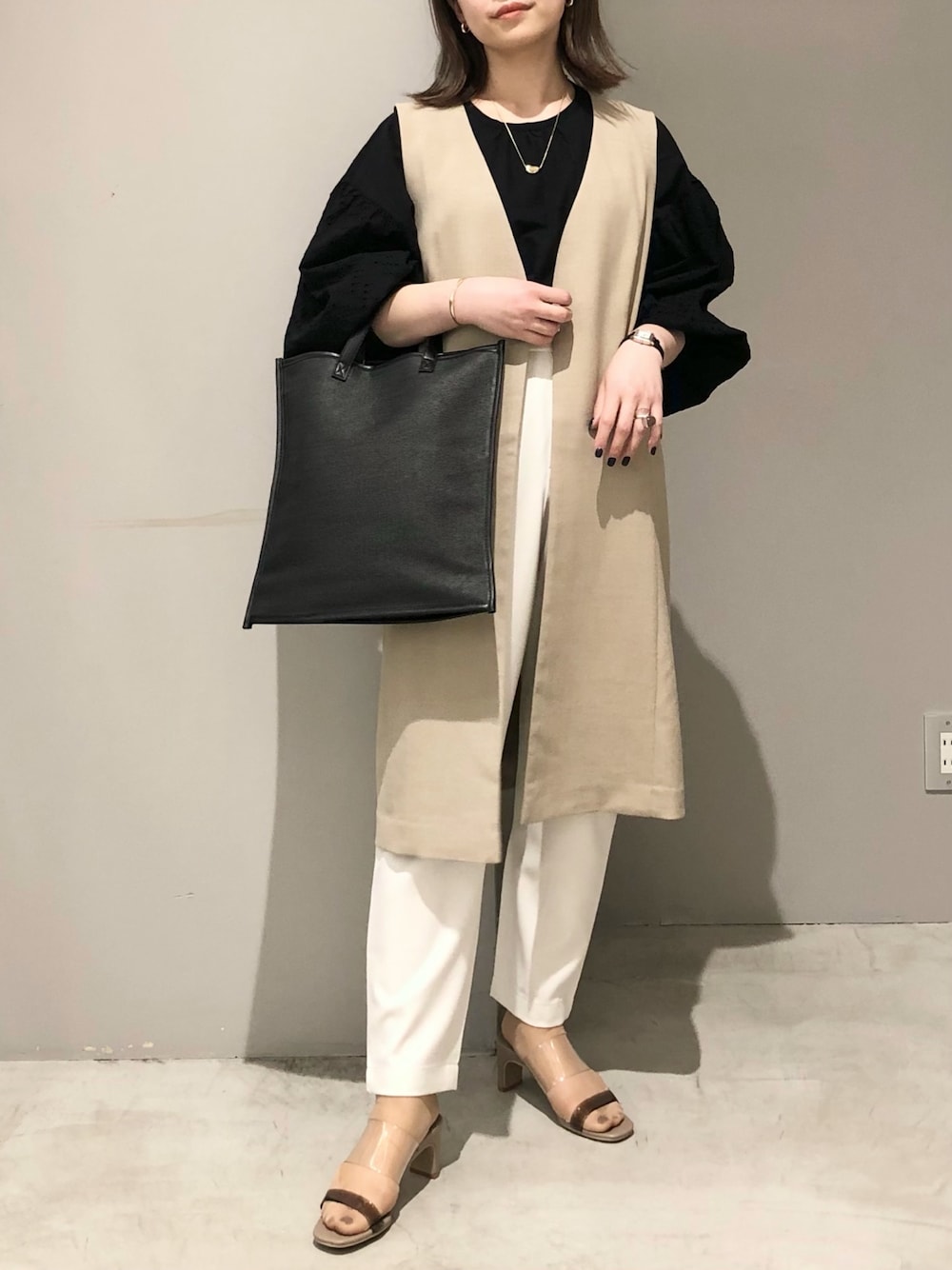 ブラック系のショルダーバッグ、ホワイト系のスラックス、ベージュ系のサンダルを着用したレディースの春コーディネートの1枚目の写真