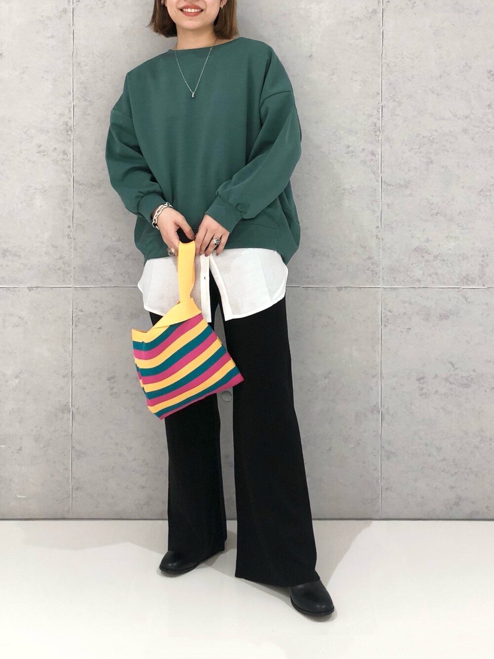イエロー系のハンドバッグ、ブラック系のパンツ、グリーン系のスウェットを着用したレディースの冬コーディネートの2枚目の写真