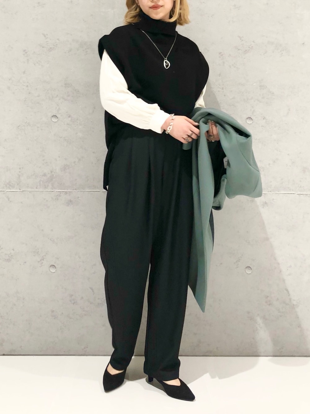 グリーン系のノーカラーコート、ブラック系のパンツ、ブラック系のパンプスを着用したレディースの冬コーディネートの2枚目の写真