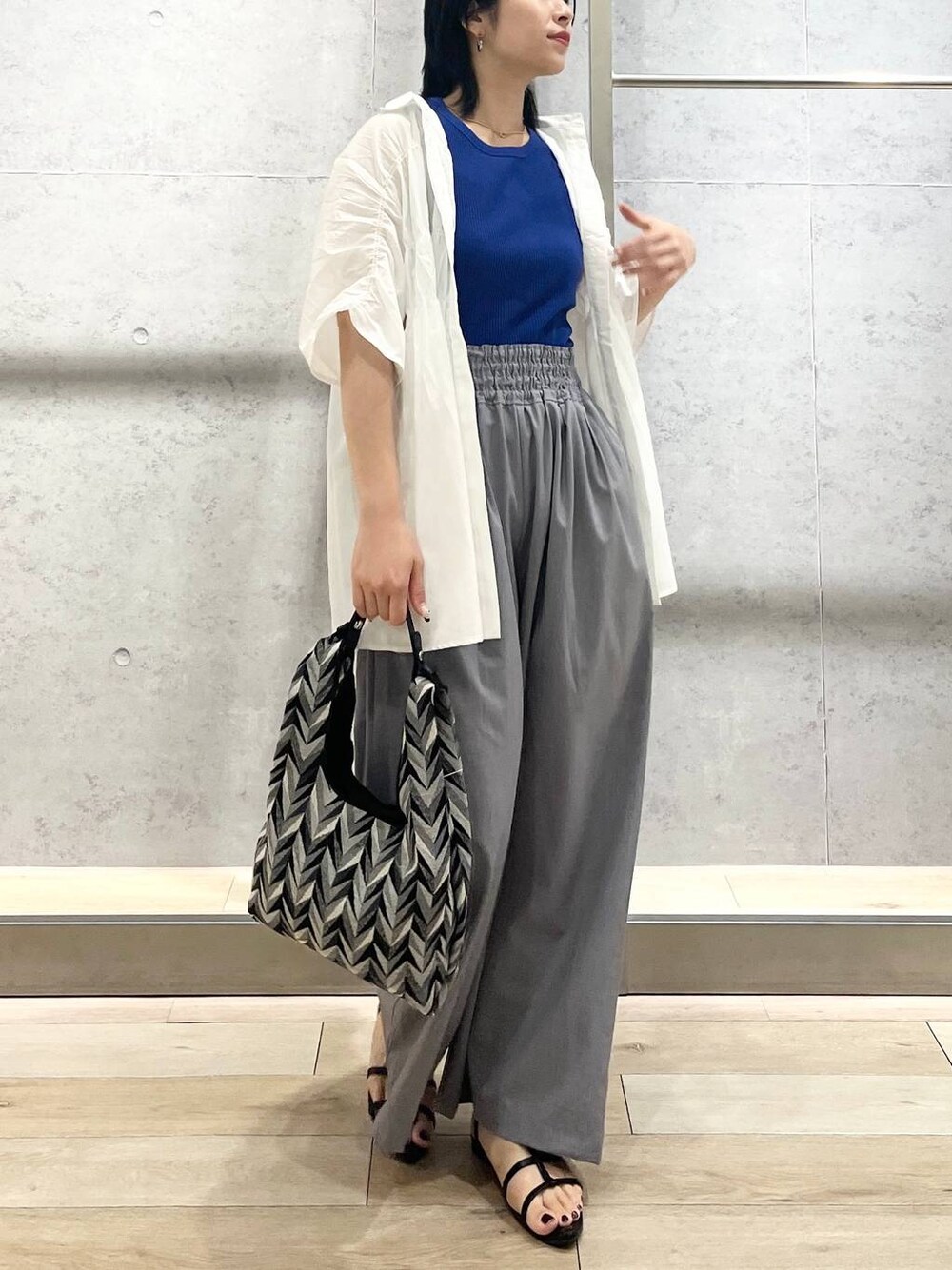 ブラック系のサンダル、ブラック系のハンドバッグ、グレー系のスラックスを着用したレディースの夏コーディネートの1枚目の写真