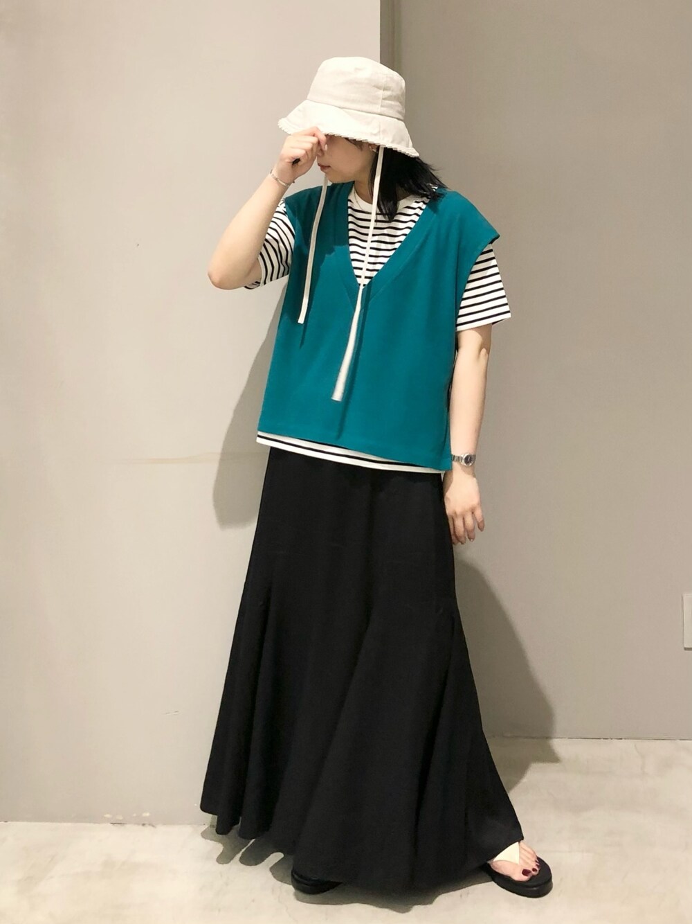 ホワイト系のサンダル、ブラック系のスカート、グリーン系のベストを着用したレディースの夏コーディネートの2枚目の写真