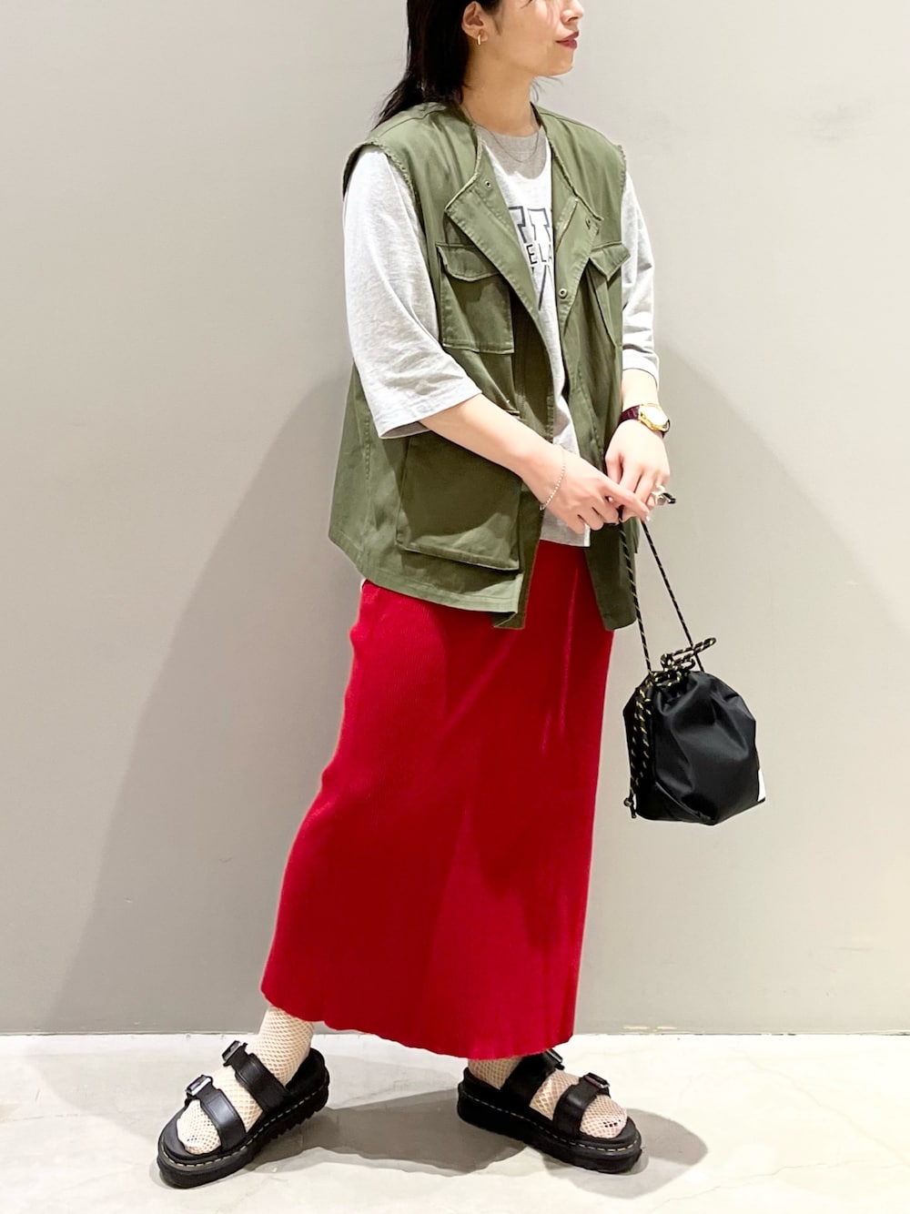レッド系のスカート、ブラック系のサンダル、ブラック系のショルダーバッグを着用したレディースの秋コーディネートの1枚目の写真