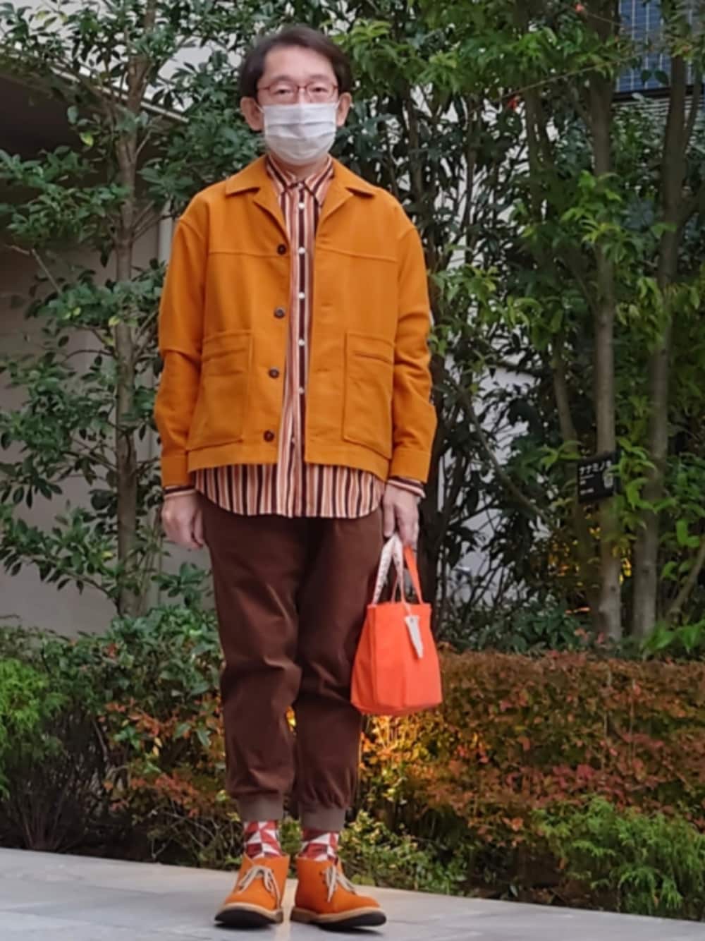 オレンジ系のブーツ、オレンジ系のトートバッグ、ブラウン系のパンツを着用したメンズの秋コーディネートの1枚目の写真