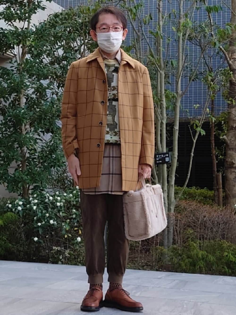 ベージュ系のハンドバッグ、グリーン系のパンツ、ブラウン系のドレスシューズを着用したメンズの春コーディネートの1枚目の写真