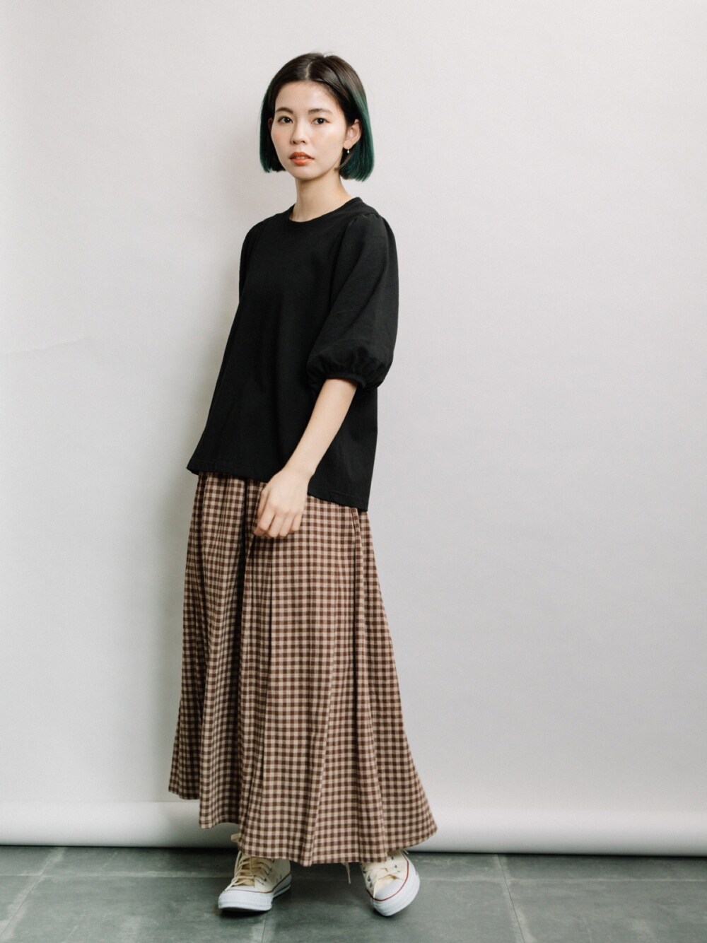 ブラック系のTシャツ/カットソー、ブラウン系のスカート、ホワイト系のスニーカーを着用したレディースの春コーディネートの1枚目の写真