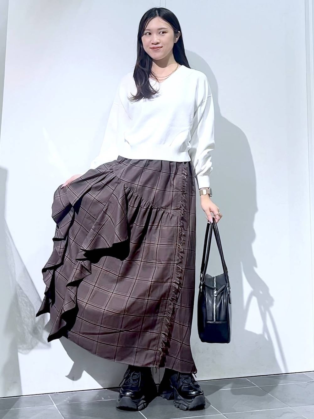 ブラック系のスニーカー、ブラック系のボストンバッグ、ホワイト系のニット/セーターを着用したレディースの秋コーディネートの1枚目の写真