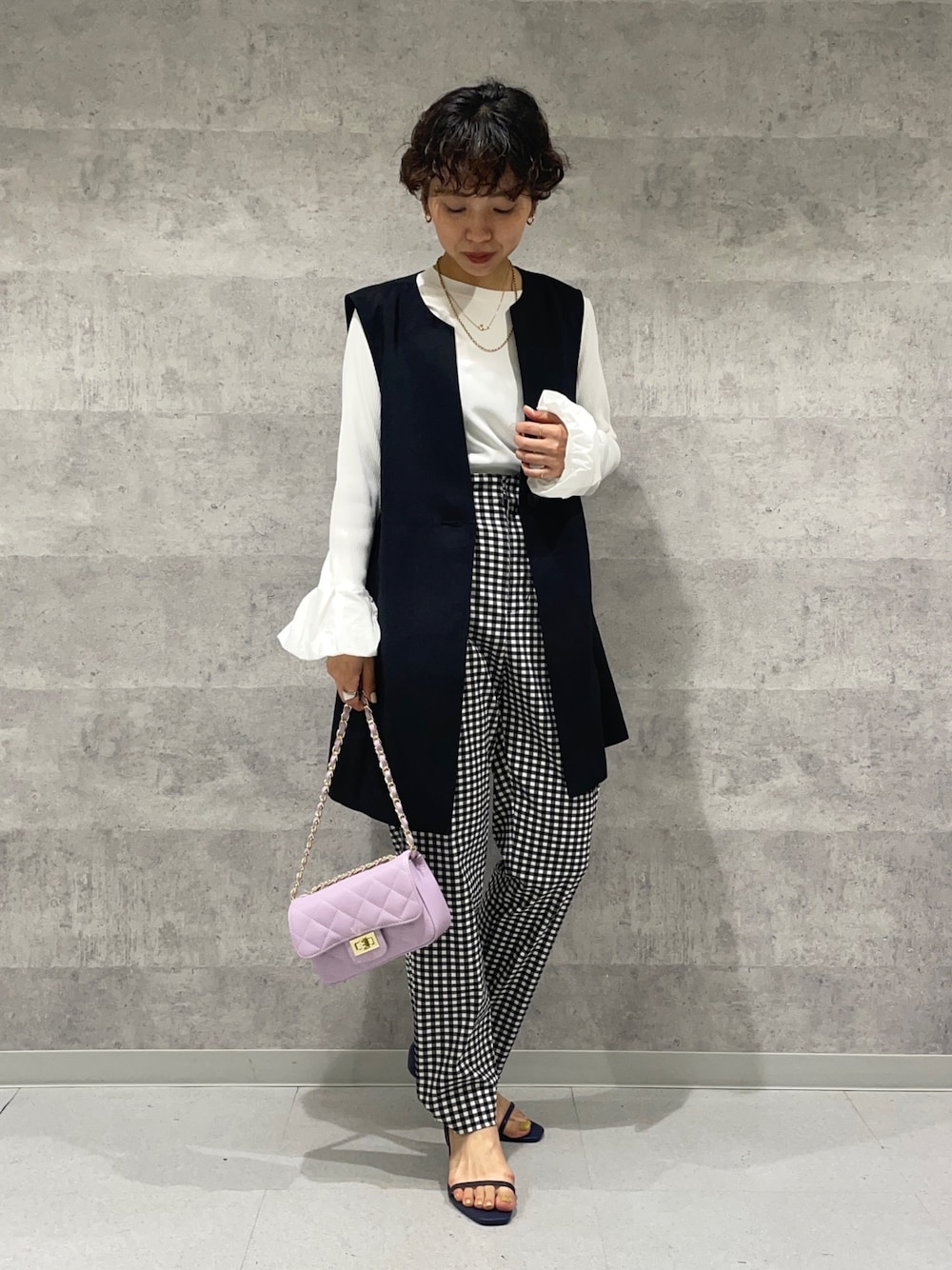 ブラック系のベスト、ホワイト系のニット/セーター、パープル系のショルダーバッグを着用したレディースの春コーディネートの1枚目の写真