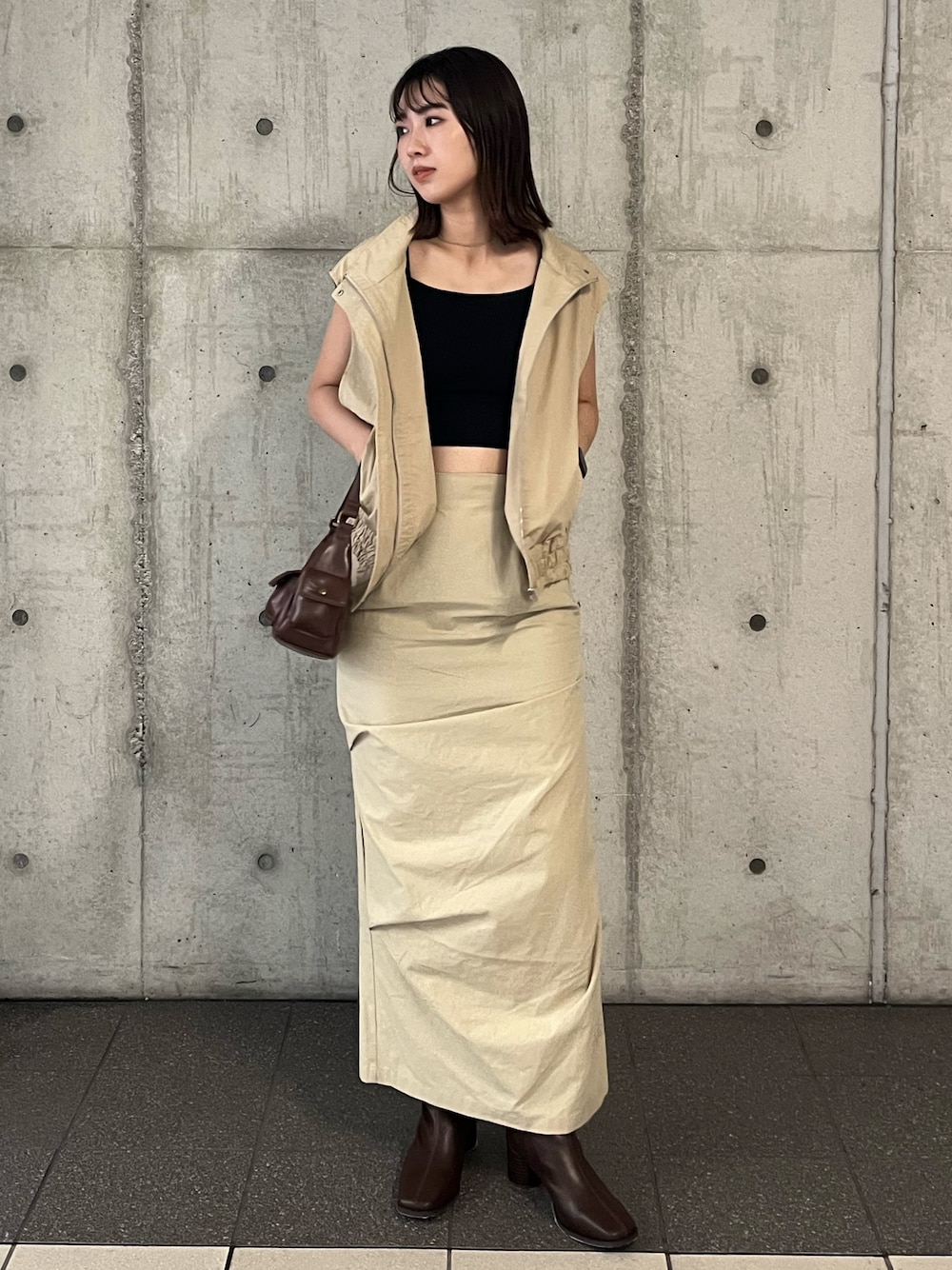 ベージュ系のベスト、ベージュ系のスカート、ブラウン系のハンドバッグを着用したレディースの夏コーディネートの1枚目の写真