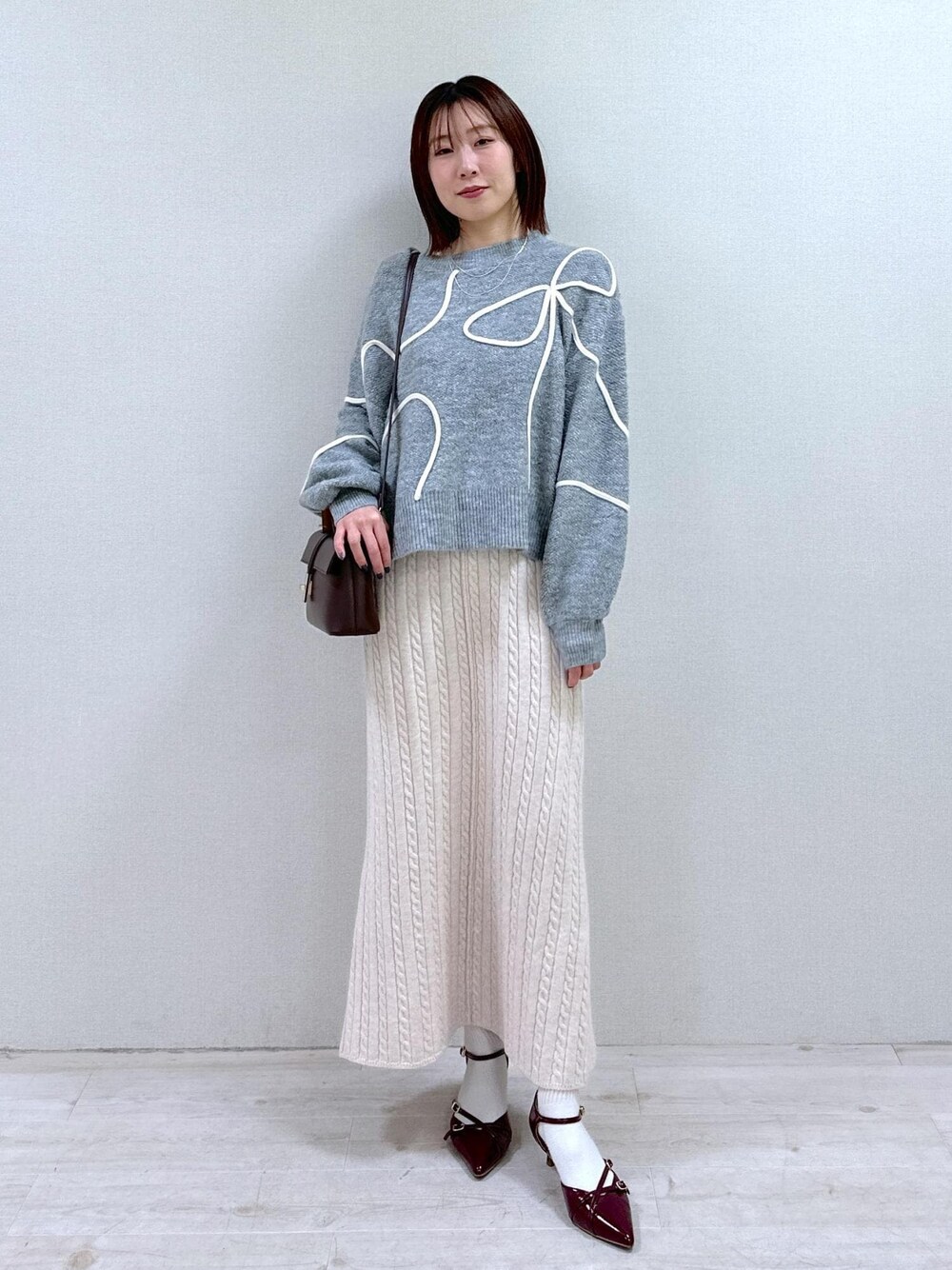 レッド系のパンプス、グレー系のニット/セーター、ブラウン系のショルダーバッグを着用したレディースの冬コーディネートの1枚目の写真