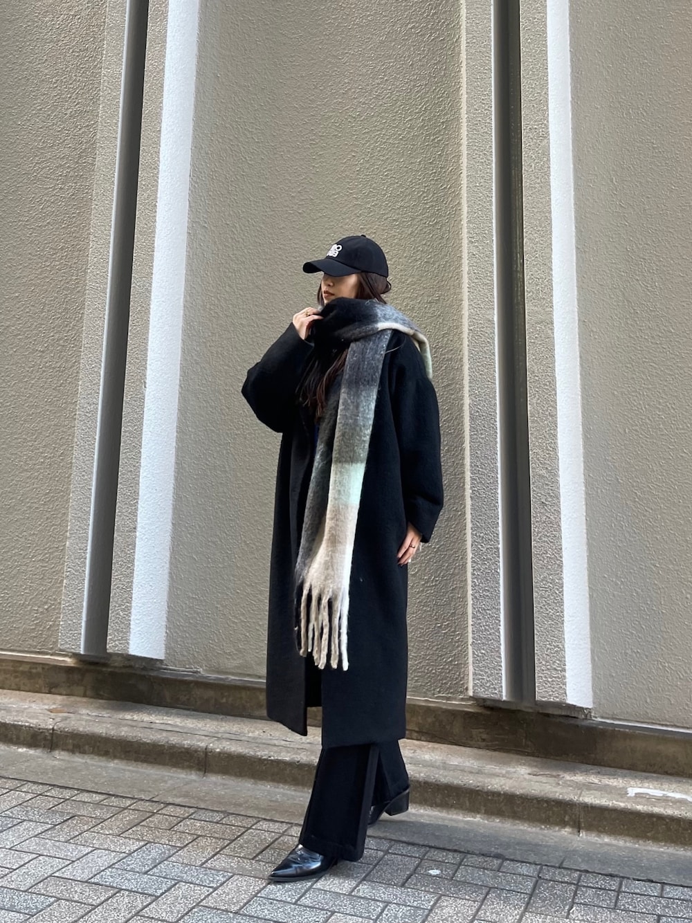 ブラック系のチェスターコート、ブラック系のデニムパンツ、ブラック系のマフラーを着用したレディースの冬コーディネートの1枚目の写真