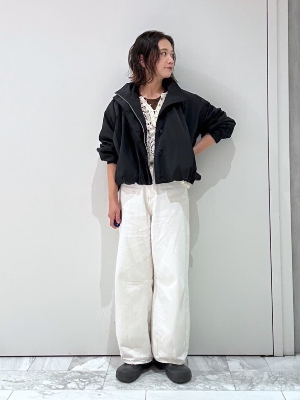 ブラック系のブルゾン、ホワイト系のニット/セーター、ホワイト系のデニムパンツを着用したレディースの夏コーディネートの1枚目の写真