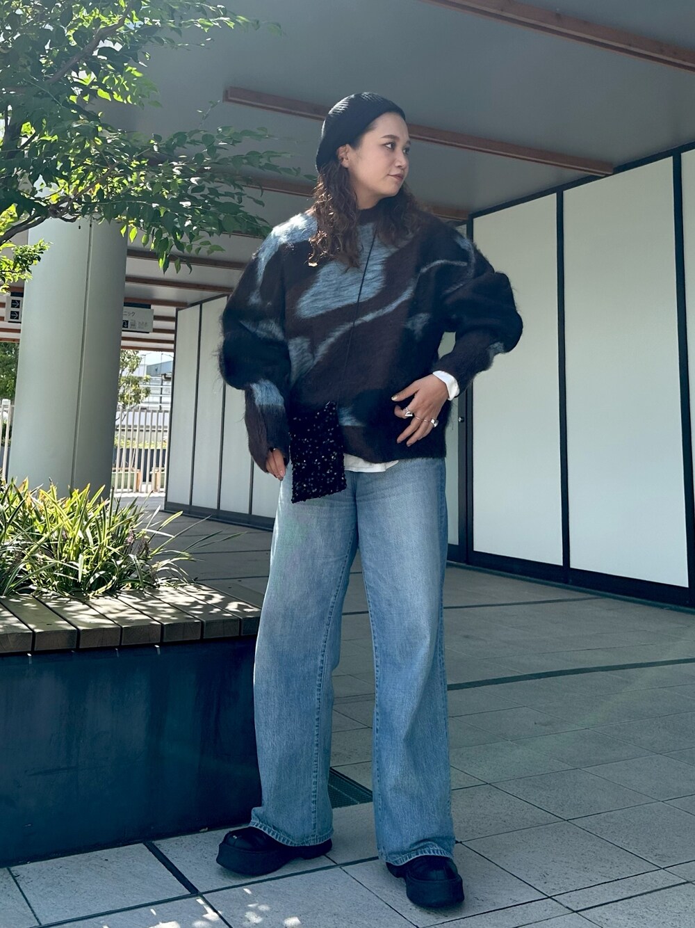 ブラウン系のニット/セーター、ブラック系のショルダーバッグ、ブルー系のデニムパンツを着用したレディースの秋コーディネートの1枚目の写真