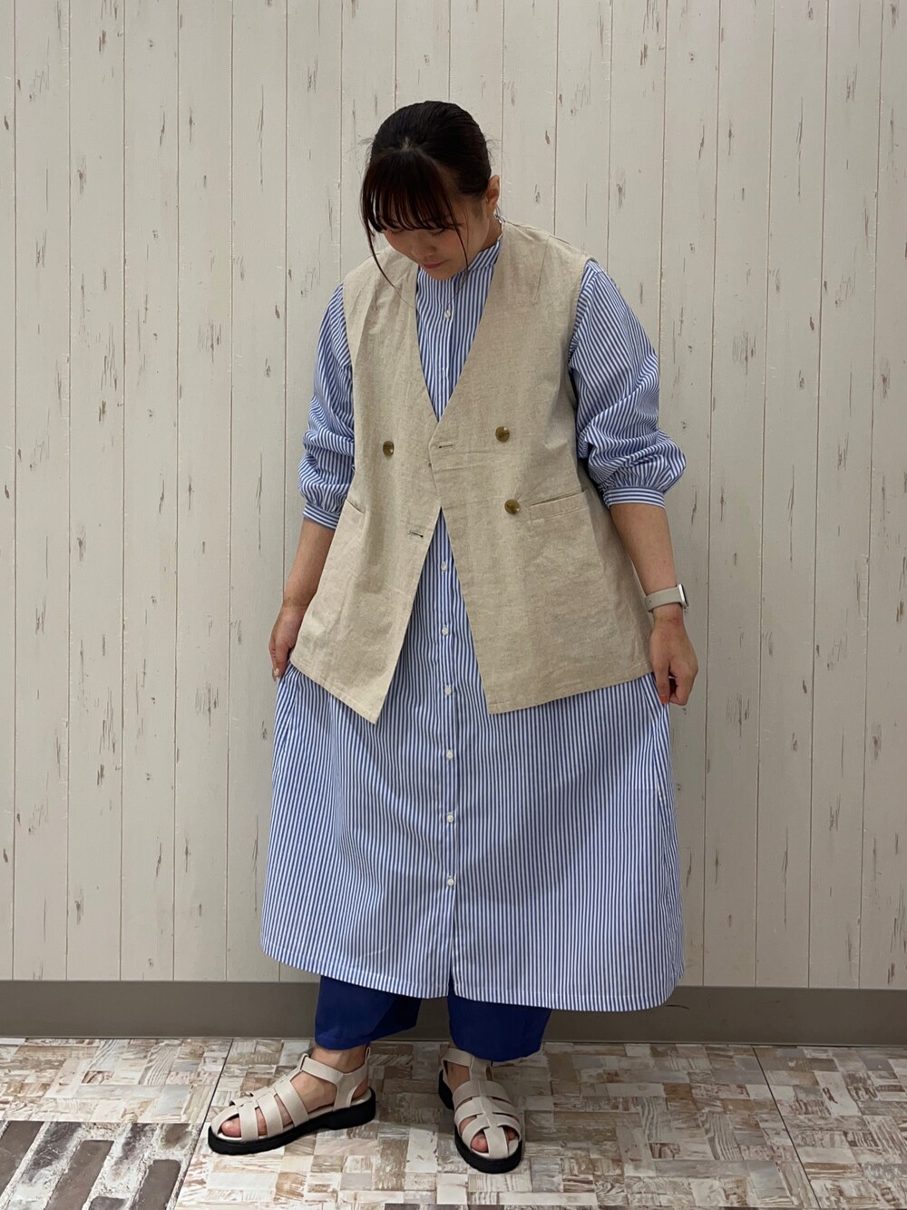 ホワイト系のベスト、ブルー系のシャツワンピース、ホワイト系のサンダルを着用したレディースの春コーディネートの1枚目の写真