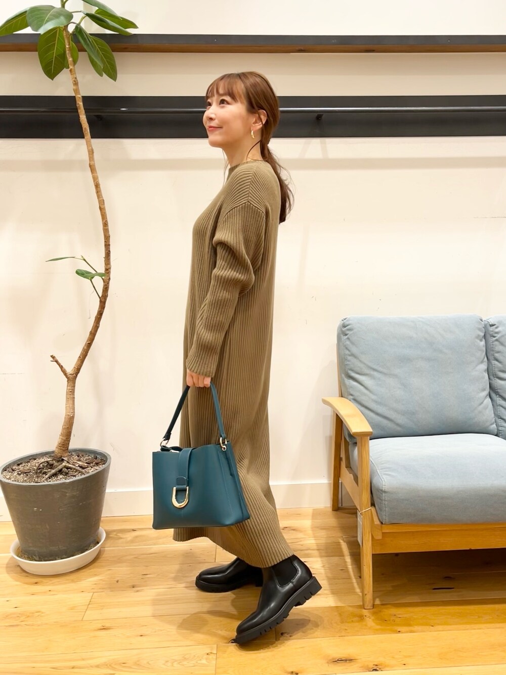 ブラウン系のワンピース、ブルー系のハンドバッグ、ブラック系のブーツを着用したレディースの冬コーディネートの1枚目の写真