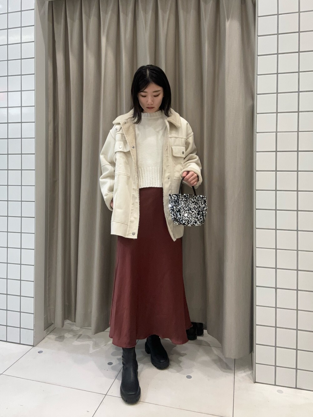 ホワイト系のニット/セーター、ブラウン系のスカート、シルバー系のハンドバッグを着用したレディースの冬コーディネートの1枚目の写真