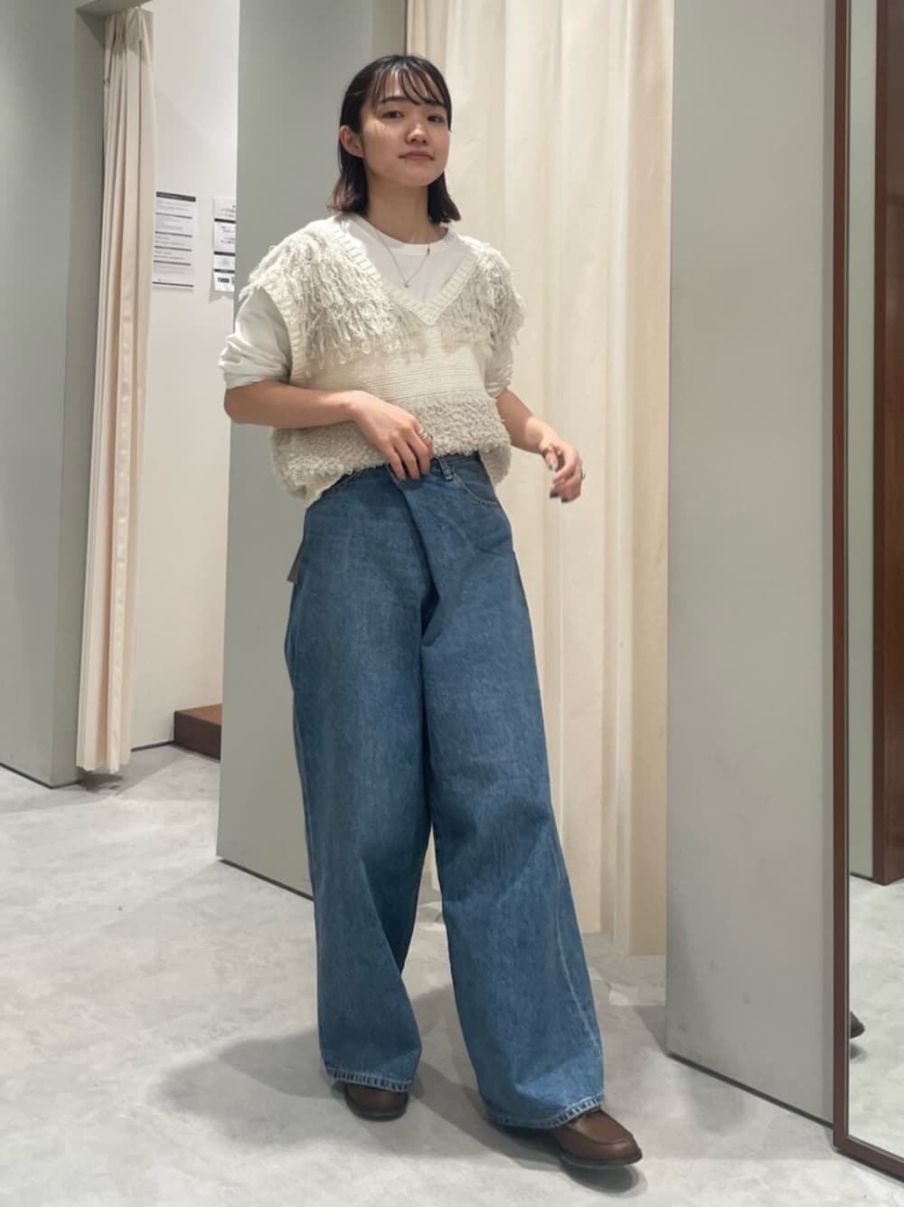 ホワイト系のベスト、ブルー系のデニムパンツ、ブラウン系のローファーを着用したレディースの春コーディネートの1枚目の写真