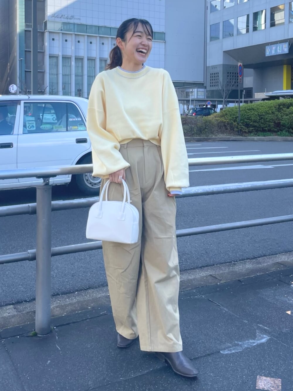 イエロー系のニット/セーター、ベージュ系のチノパンツ、ホワイト系のボストンバッグを着用したレディースの冬コーディネートの1枚目の写真