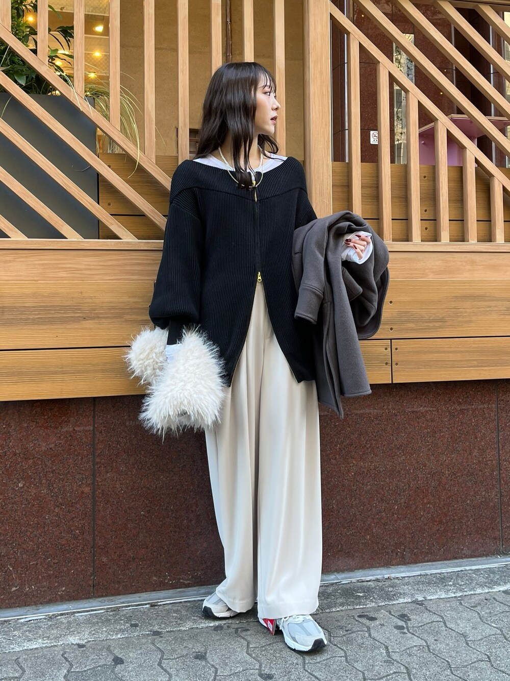 グレー系のスラックス、ブラック系のニット/セーター、ホワイト系のTシャツ/カットソーを着用したレディースの冬コーディネートの1枚目の写真