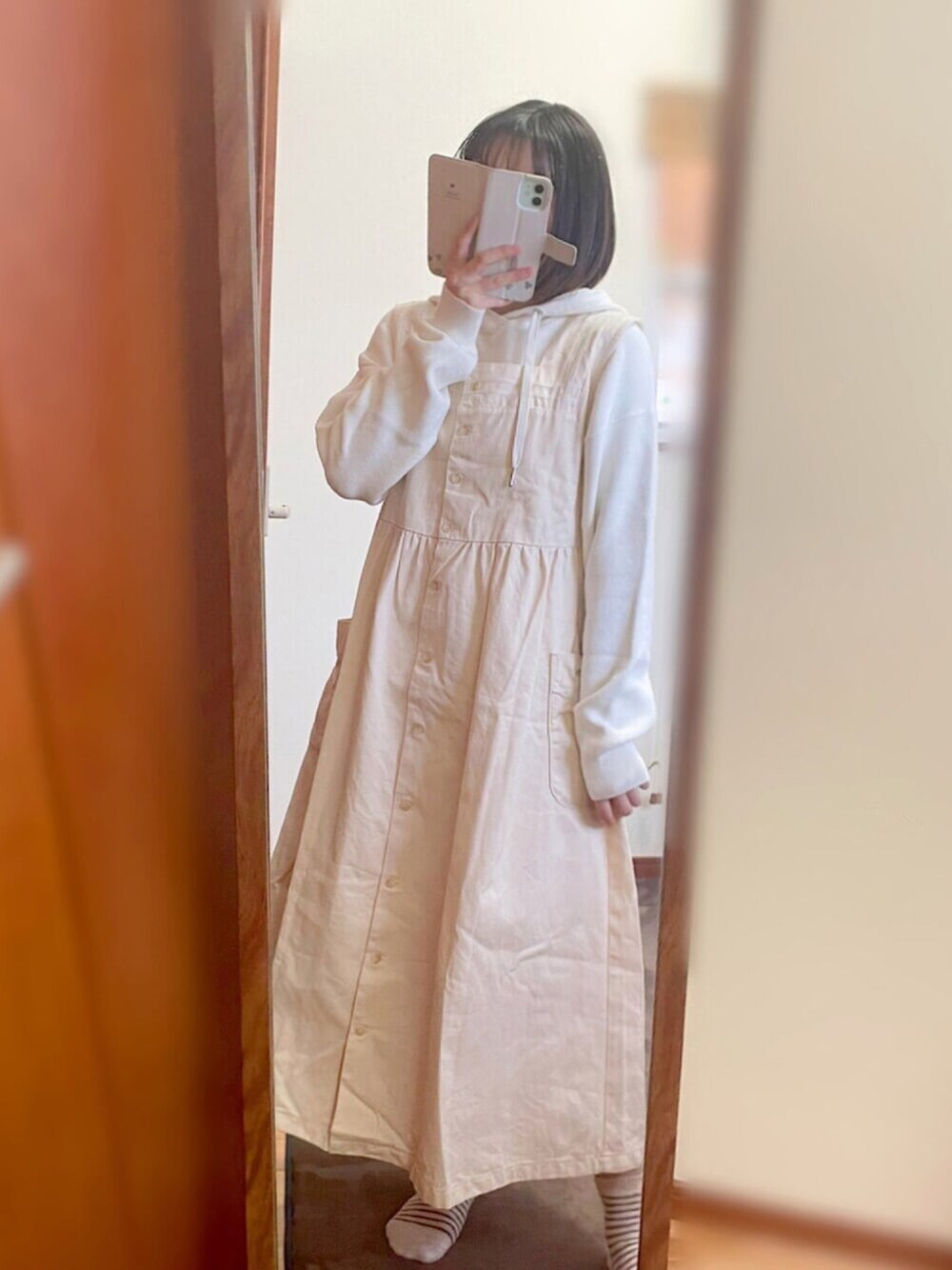 ホワイト系のジャンパースカート、ホワイト系のニット/セーター、グレー系のステンカラーコートを着用したレディースの冬コーディネートの1枚目の写真