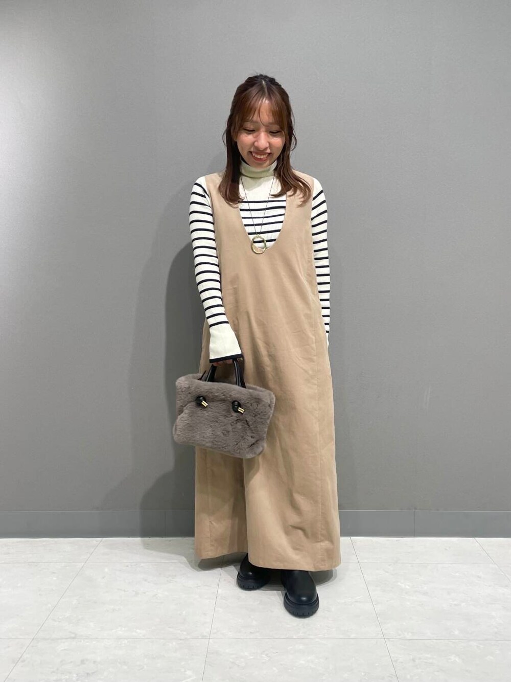 ホワイト系のニット/セーター、ベージュ系のワンピース、ブラック系のブーツを着用したレディースの秋コーディネートの1枚目の写真