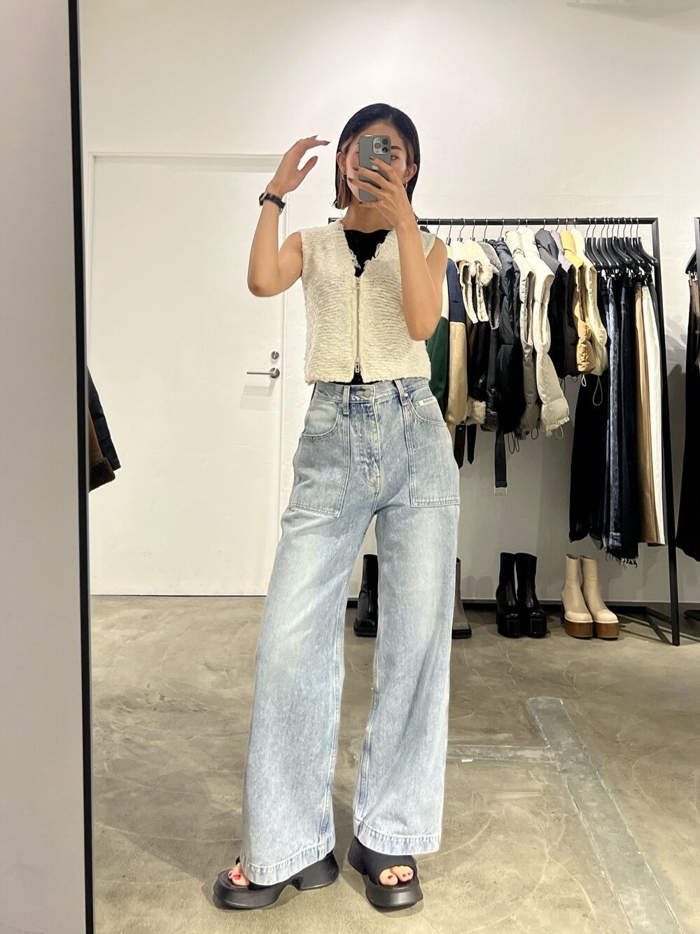 ブルー系のデニムパンツ、ホワイト系のベスト、ブラック系のサンダルを着用したレディースの夏コーディネートの1枚目の写真