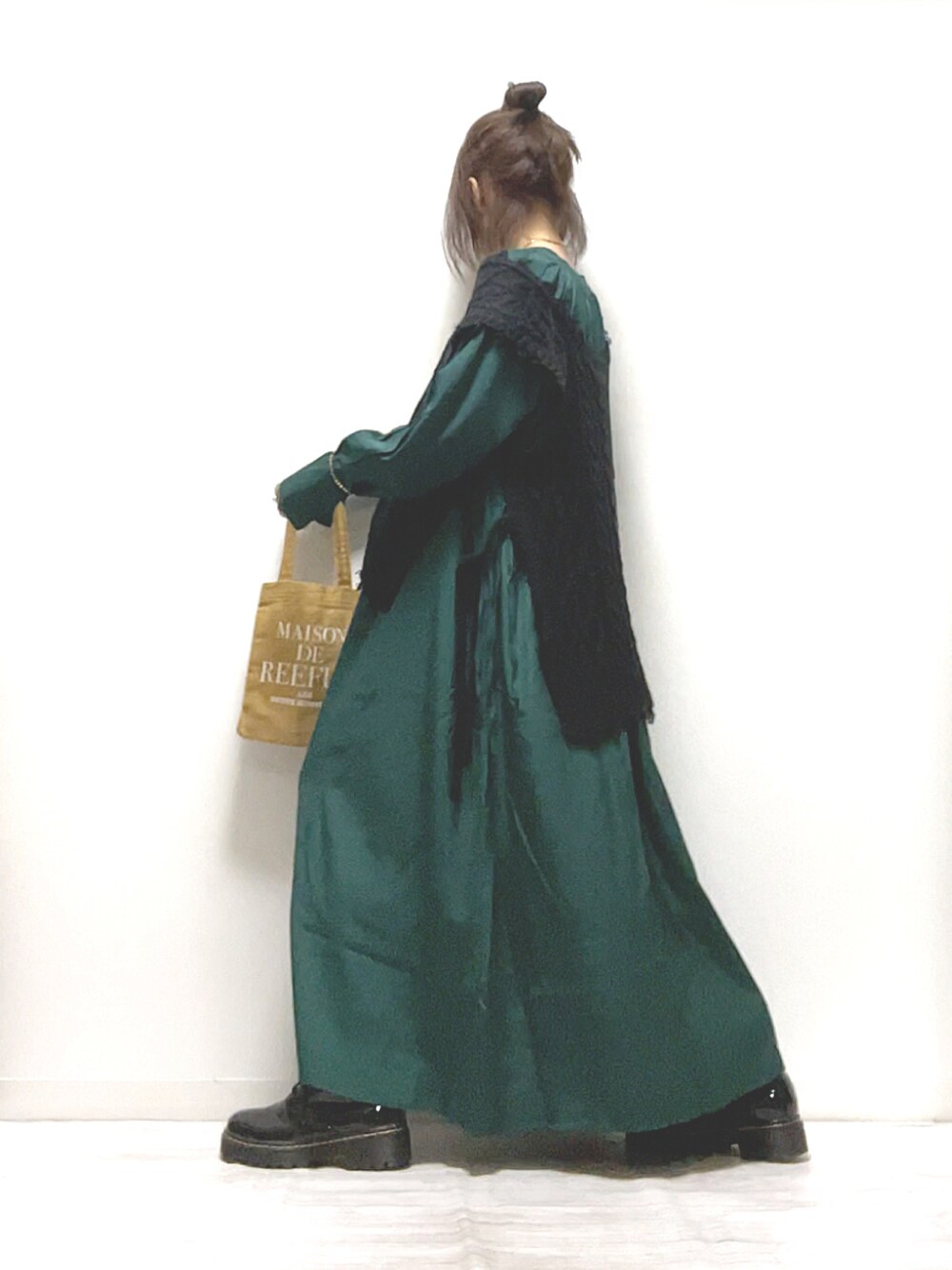 グリーン系のワンピース、ブラック系のベスト、ブラック系のブーツを着用したレディースの秋コーディネートの1枚目の写真